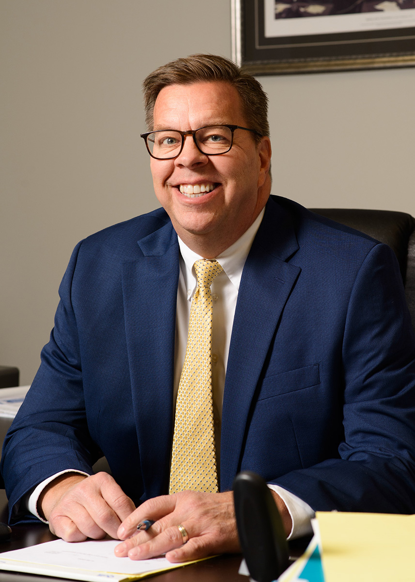 Scott Becker at a desk with pen in hand ready to sign a paper.